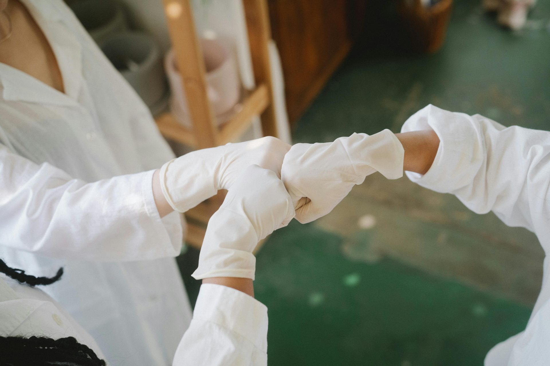 Nahaufnahme von medizinischem Fachpersonal in weißen Laborkitteln und Handschuhen, die sich in einer Laborumgebung die Fäuste geben.